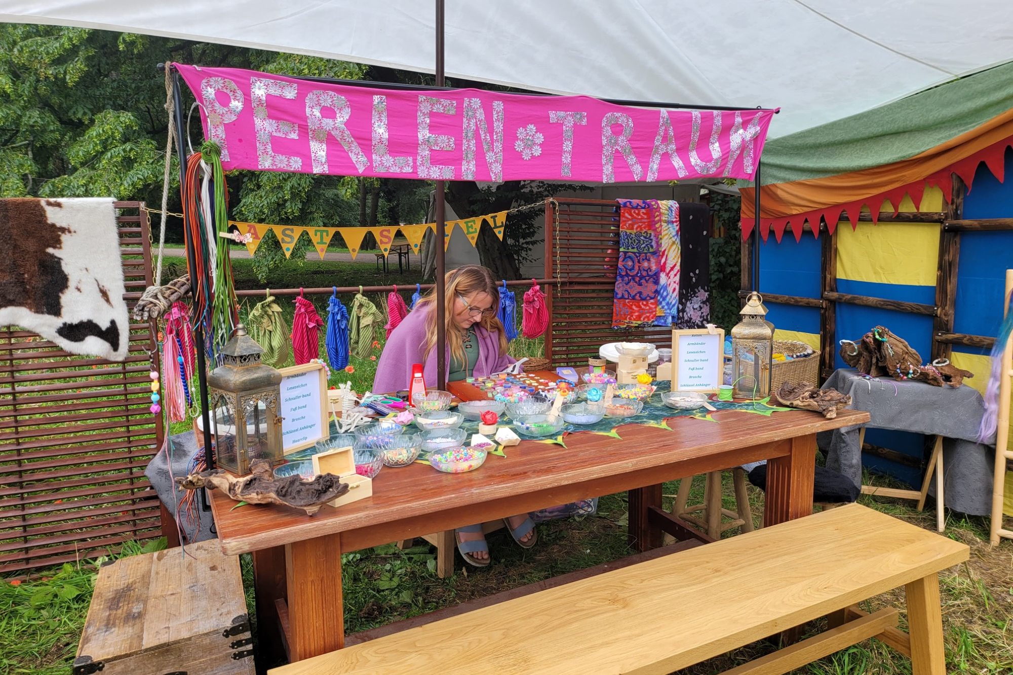 Verkaufstisch mit bunten Perlen und einer Verkäuferin, umgeben von festlichen Dekorationen.