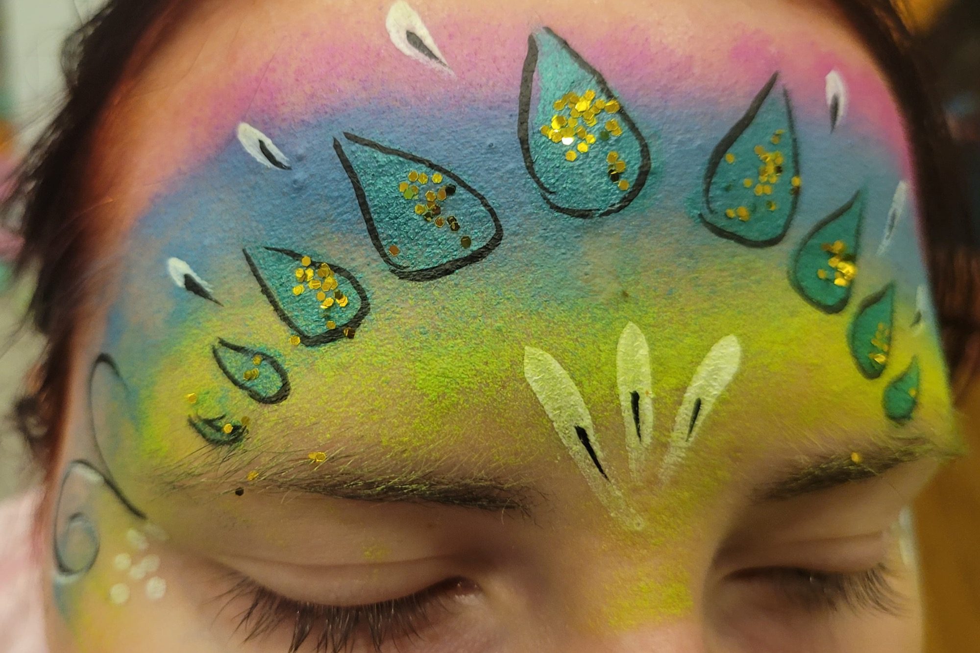 Bunte Gesichtsmalerei mit Wassertropfen und goldenen Akzenten auf der Stirn.
