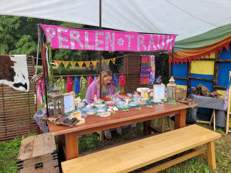 Stand mit bunten Schmuckperlen, Verkäuferin und fröhlicher Marktatmosphäre.