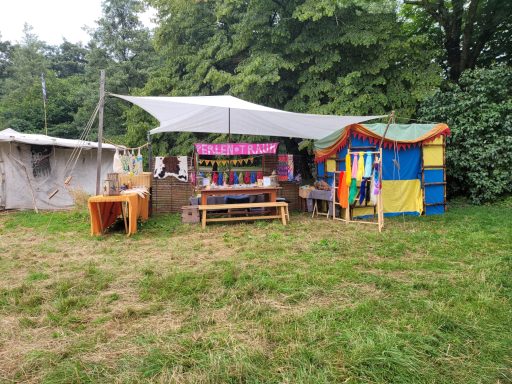 Bunte Marktstände mit Tischen und Sonnenschutz in einer grünen Wiese.