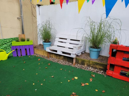 Bunte Dekoration mit einer weißen Holzbank, Pflanzen in Töpfen und farbigen Paletten.