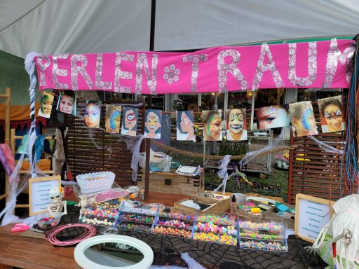 Marktbude mit buntem Banner und Schmuckstücken, einschließlich Perlen und Porträts.