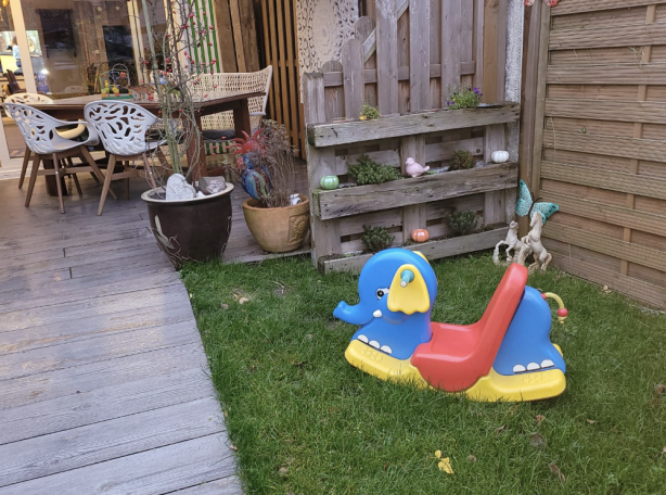 Buntes Wippgerät in einem Garten mit Holzzäunen und Sitzgelegenheiten im Hintergrund.