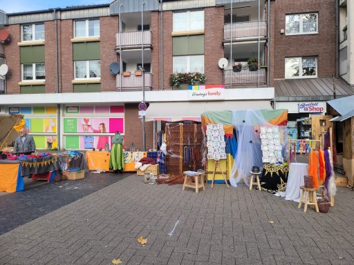 Markt mit bunten Ständen und Kleidung vor einem Wohngebäude.