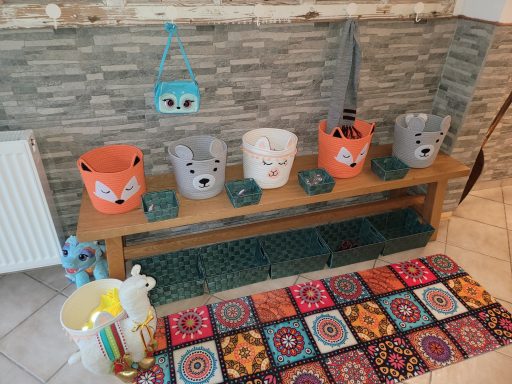 Bunte Aufbewahrungskörbe mit Tiermotiven auf einer Holzbank, farbenfrohe Teppichunterlage.