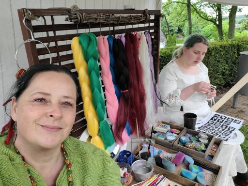 Zwei Frauen mit Handarbeitsmaterialien, eine lächelt in die Kamera, die andere arbeitet.