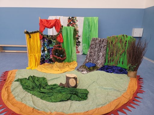 Bunte Kulisse mit Stoffen, einem Baumstumpf und grünen Elementen für eine Inszenierung.