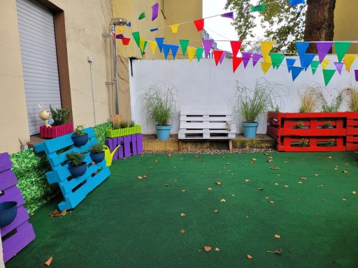 Bunte Holzbänke und Töpfe umgeben von grüner Rasenfläche und Girlanden.