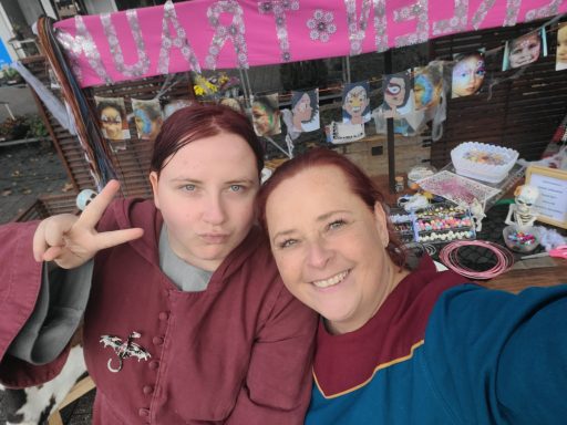 Zwei Frauen in historischen Gewändern lächeln und posieren mit einem Frieden-Zeichen.