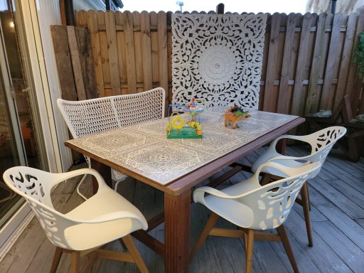 Holztisch mit dekorativem Kachelmuster und weißen Stühlen auf einer Terrasse.