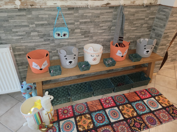 Bunte Aufbewahrungseimer mit Tiermotiven auf einer Holzbank, neben einem gemusterten Teppich.