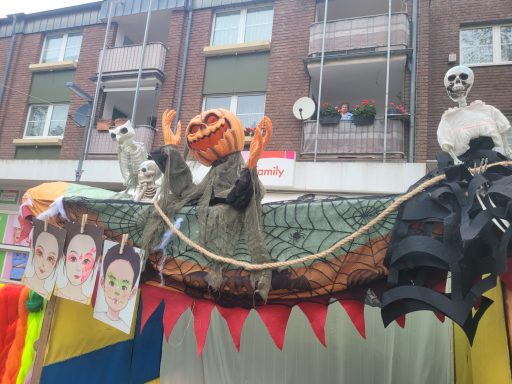 Skelettfiguren und eine Kürbis-Deko auf einem Festwagen mit bunten Bannern.