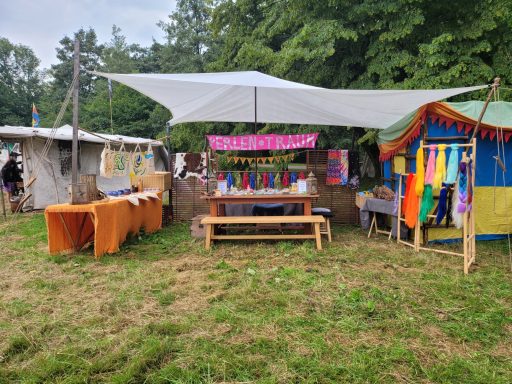 Bunt dekorierte Marktstände unter einem sonnenschirm, umgeben von Grün.