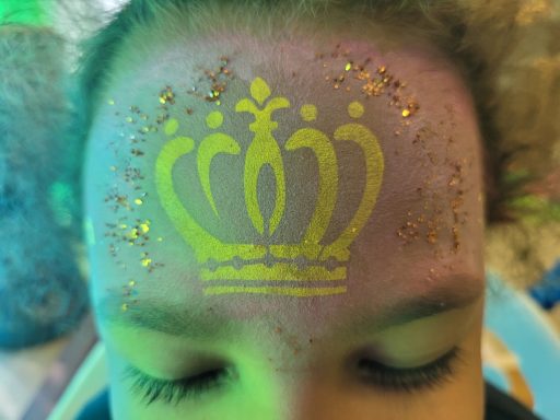 Ein Kind mit einem goldenen Krone-Tattoo und funkelndem Glitzer auf der Stirn.