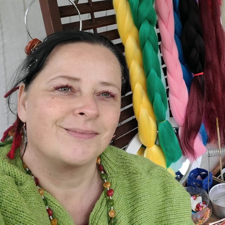 Frau mit grünem Pullover und bunten Haarsträhnen im Hintergrund.