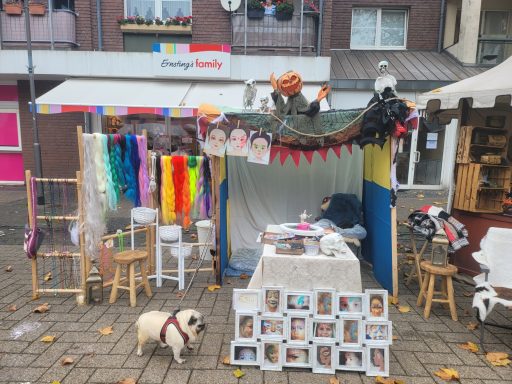 Marktstand mit bunten Stoffen, Accessoires und Fotos von Hunden, darüber ein Hund.