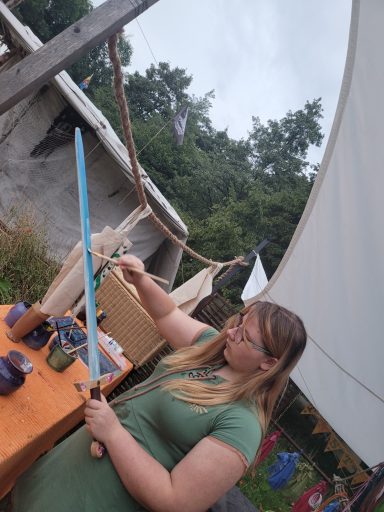 Junge Frau mit Lichtschwert vor einem Zelt und Wäscheleine im Freien.