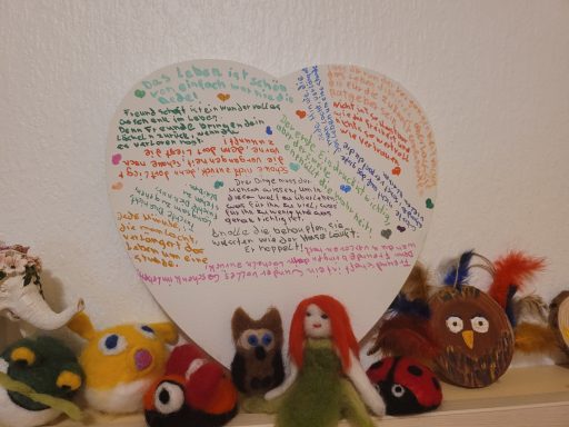 Herz aus Papier mit bunten Notizen und darauf befestigten, niedlichen handgefertigten Figuren.