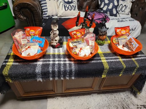 Drei orangefarbene Schüsseln mit Snacks und Süßigkeiten auf einem Tisch mit Decke.