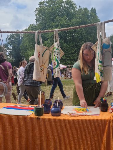 Frau gestaltet Taschen an einem Stand, im Hintergrund Menschen und grüne Bäume.