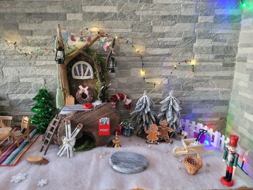 Weihnachtliche Szenerie mit einem Häuschen, Tannenbäumen und festlichen Dekorationen.