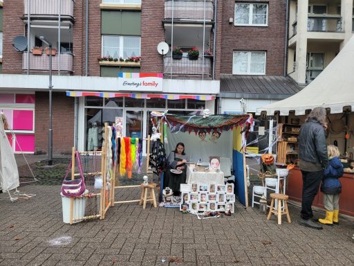 Marktstand mit Kunsthandwerk, bunten Tüchern und Besuchern in einer urbanen Umgebung.