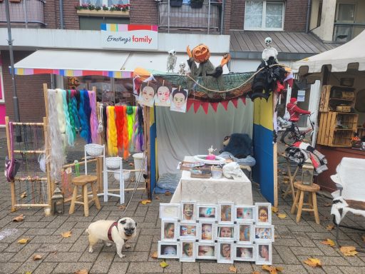 Marktstand mit bunten Stoffen, Dekoration und einem kleinen Hund auf dem Boden.