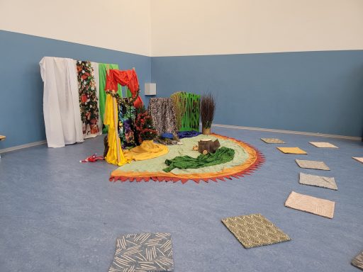 Bunte Tücher und Matten bilden eine kreative Spiel- und Entspannungsecke im Raum.